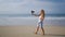 Female travel influencer records on pro camera with wireless lav mic on sandy beach. Curly-haired woman creates content