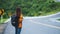 A female traveler with backpack walking along a curved and winding asphalt road in high mountains