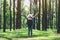 Female traveler with a hat and backpack standing back and open arms in a beautiful pine woods