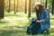 A female traveler with a hat opening her backpack while traveling in a beautiful pine woods