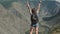 A female traveler with a rucksack climbs to the top of the mountain and raises his hands up, feeling a sense of diving