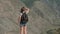 Female traveler with a rucksack stands on top of a mountain and looks ahead