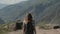 A female traveler with a rucksack walks through the mountains to the top.