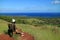 Female traveler sitting on the wooden bench admiring the aerial view of Hanga Roa and Pacific ocean, Easter island, Chile