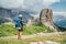 Female trekker walking with backpack and trekking poles by green mountain hill and enjoying the picturesque Dolomite Alps Cinque