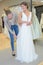 Female trying wedding dress in shop with women assistant