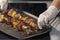 Female using gloves picking up a smoking beef skewer from a roasting tray