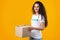 Female Volunteer Holding Donation Cardboard Box Standing On Yellow Background