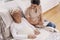 Female volunteer reads a book to an elderly woman lying in a bed