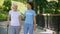 Female volunteer and senior patient with stick walking hospital garden, care