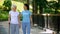 Female volunteer and senior patient with stick walking hospital garden, care