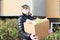 Female volunteer wearing a protective mask walks down the street with a box of groceries, donations