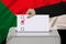 Female voter lowers the ballot in a transparent ballot box on the background of the national flag of Sudan, concept of state