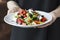 The female waiter holding in her hands plate with greek salad