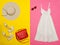 Female wardrobe. White sundress, handbag, white shoes and a hat. Bright pink-yellow background.