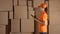 Female warehouse worker in orange uniform counting boxes and making records against brown cartons. 4K studio lighting