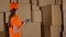 Female warehouse worker in orange uniform counting boxes and using her tablet against brown cartons backround. 4K video