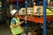 Female warehouse worker wearing hardhats and reflective jackets checking inventory boxes with barcode scanner