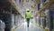 Female warehouse worker wearing helmet checks walks in storehouse, storeroom with rows of shelves