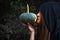 Female wizard kissing pumpkin lantern. Female costume in black clothes and hood on mystery forest background. Halloween day and