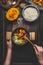 Female women hands holding pot and spoon and cooking pumpkin risotto on dark rustic kitchen table with ingredients, top view. Clea