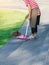 Female worker sweeping yard with broom tool and dustpan in ornamental backyard garden. Woman wear apron with hat sweeping away