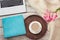 Female workplace with a laptop, cup of coffee, blue notebook, cozy sweater and pink flowers on wooden background.Top view composit