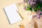 Female workspace with paper notebook, golden pen, silk scarf, accessories, purple lilac flowers on beige pastel color background.