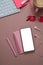 Female workspace with smart phone, earphone, notebook and keyboard on pastel pink background.