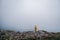 Female in yellow raincoat, jeans shorts standing at top of mountain with view of peaks at horizon. Landscape. Nature.