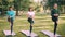 Female yoga students are doing balancing exercise standing on one leg on mats in park, girls are training under guidance