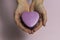 In female young hands lies a small heart-shaped box, close-up, on a light pinkish background