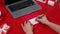 Females hands write Happy Women's Day in red marker on the greeting postcard. Top view of a red table with a laptop and