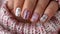 Feminine hand showcasing sophisticated white glitter nail art paired with a delicate pastel sweater