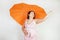 Feminine woman with plus size body in pink dress with orange big heart shaped umbrella posing on white background in Studio