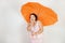 Feminine woman with plus size body in pink dress with orange big heart shaped umbrella posing on white background in Studio