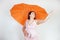 Feminine woman with plus size body in pink dress with orange big heart shaped umbrella posing on white background in Studio