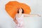 Feminine woman with plus size body in pink dress with orange big heart shaped umbrella posing on white background in Studio