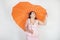 Feminine woman with plus size body in pink dress with orange big heart shaped umbrella posing on white background in Studio