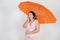 Feminine woman with plus size body in pink dress with orange big heart shaped umbrella posing on white background in Studio