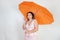 Feminine woman with plus size body in pink dress with orange big heart shaped umbrella posing on white background in Studio