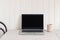 Feminine workspace composition with open laptop. Ceramic vase on beige linen tablecloth. White wooden wall background