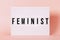 `Feminist` Luminous poster. Feminist themed letters with pink background. Feminism concept.