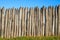 Fence made of sharp wooden stakes against the blue sky. Wooden fence vertical logs pointed against the sky protection against