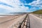 Fenced footpath on a seawall along a sandy beach wuth groynes