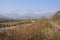 Fenced jogging path in weeds along dried riverway before broken bridge with jokul in distance