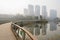 Fenced planked footbridge over water in foggy city at sunny win