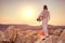 Fencer man standing on top of the rock holding fencing mask and a sword on sunset background
