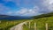 Fences with wooden posts and barbed wire on a dirt trail between the Irish countryside with a rainbow over the Atlantic Ocean