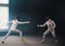 A fencing training in the studio - two women in protective costumes having a duel - pointing swords at each other